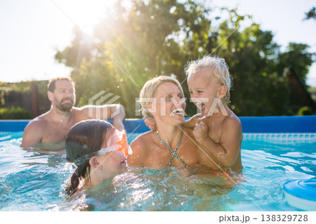 Young family with two children in swimming pool outdoors in backyard garden. Young family with two children in swimming pool outdoors in backyard garden. 138329728
