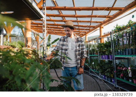 Garden center owner watering plants with hose in greenhouse. Garden center owner watering plants with hose in greenhouse. 138329739