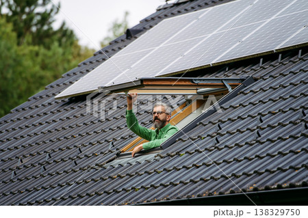 Man looking from skylight, roof window with solar panels above him. Sustainable lifestyle and green household. 138329750