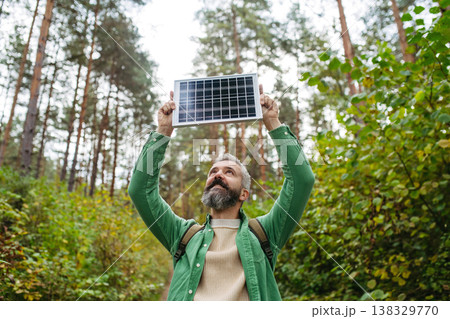 Handsome man standing in the middle of forest, holding small solar panel above his head. Handsome man standing in the middle of forest, holding small solar panel above his head. 138329770