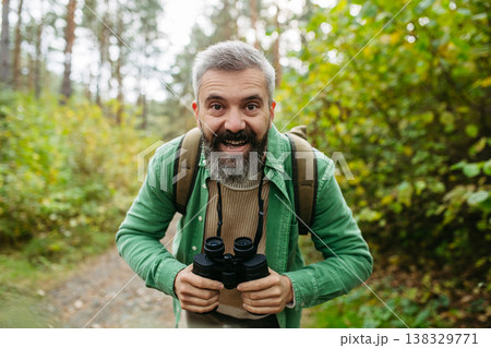 Handsome man watching wildlife with binoculars, enjoying peaceful atmosphere of forest, forestbathing 138329771