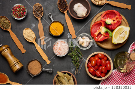 Spices, vegetables, and herbs on a dark background turmeric, pepper, salt, cloves, thyme, bay leaf, garlic, cherry tomatoes 138330033
