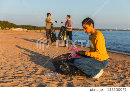 Earth day. Volunteers activists team collects garbage cleaning of beach coastal zone. Woman mans puts plastic trash in garbage bag on ocean shore. Environmental conservation coastal zone cleaning 138330071