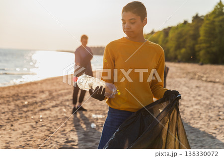 Earth day. Volunteers activists team collects garbage cleaning of beach coastal zone. Woman puts plastic bottle trash in garbage bag on ocean shore. Environmental conservation coastal zone cleaning Earth day. Volunteers activists team collects garbage cleaning of beach coastal zone. Woman puts plastic bottle trash in garbage bag on ocean shore. Environmental conservation coastal zone cleaning 138330072