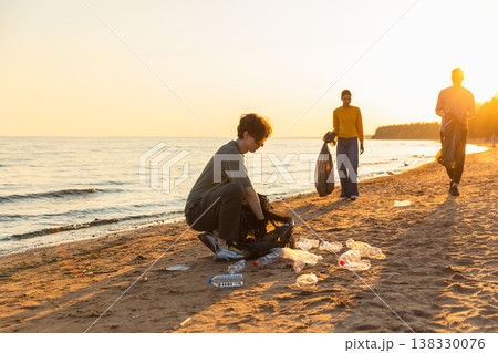 Earth day. Volunteers activists team collects garbage cleaning of beach coastal zone. Woman mans puts plastic trash in garbage bag on ocean shore. Environmental conservation coastal zone cleaning 138330076