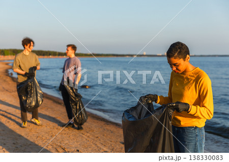 Earth day. Volunteers activists team collects garbage cleaning of beach coastal zone. Woman puts plastic bottle trash in garbage bag on ocean shore. Environmental conservation coastal zone cleaning Earth day. Volunteers activists team collects garbage cleaning of beach coastal zone. Woman puts plastic bottle trash in garbage bag on ocean shore. Environmental conservation coastal zone cleaning 138330083