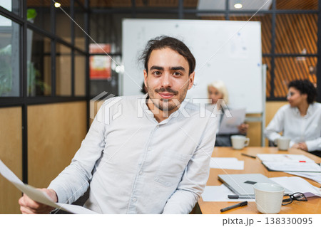 Portrait of team leader businessman in office, colleagues meeting in background. Confident business leader man sitting in office. Boss leader professional worker. Working process office life career 138330095