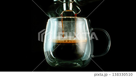 Fresh espresso pouring from coffee machine into glass cup with rich crema and rising steam. Warm cinematic scene capturing preparation of black coffee in cozy atmosphere. 138330510