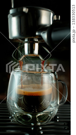 Fresh espresso pouring from coffee machine into glass cup with rich crema and rising steam. Warm cinematic scene capturing preparation of black coffee in cozy atmosphere. Fresh espresso pouring from coffee machine into glass cup with rich crema and rising steam. Warm cinematic scene capturing preparation of black coffee in cozy atmosphere. 138330513