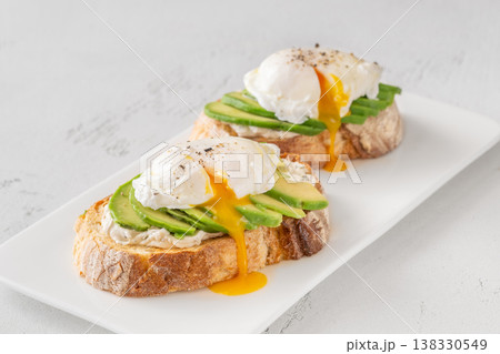 Avocado toast with poached eggs and runny yolk on artisan bread plate 138330549