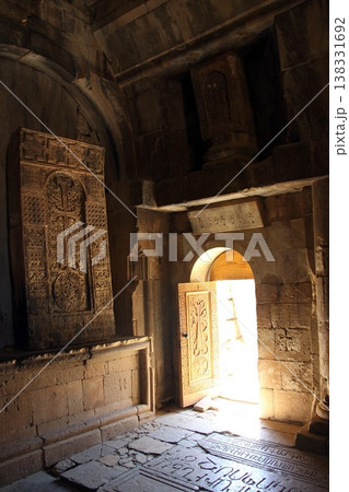 Warm sunlight streams through the open doors of an ancient stone church, illuminating the historic walls and stone floor. 138331692