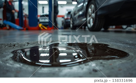 A close-up of a dark oil spill on the floor of an auto repair shop with a car in the background. Concepts of industrial work, maintenance issues, workplace safety, and environmental hazards. A close-up of a dark oil spill on the floor of an auto repair shop with a car in the background. Concepts of industrial work, maintenance issues, workplace safety, and environmental hazards. 138331696
