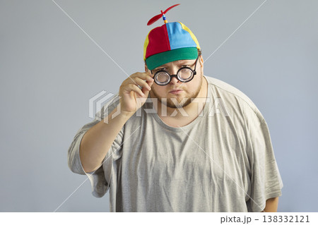 Funny overweight man in propeller cap adjusting glasses, playful comic pose 138332121