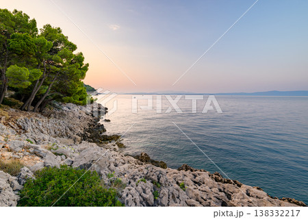 Tranquil rocky coastline at sunset with calm sea 138332217
