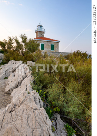Stone lighthouse on rocky coastal hillside at dusk 138332227