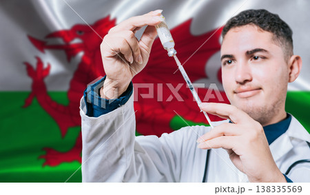 Doctor holding syringe on Wales flag background. Medical professional holding syringe with Welsh flag in the background Doctor holding syringe on Wales flag background. Medical professional holding syringe with Welsh flag in the background 138335569