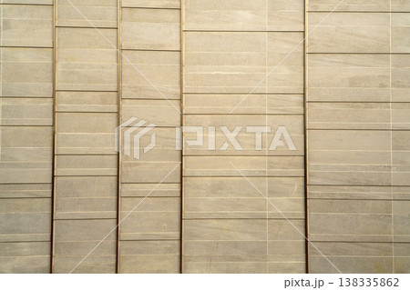 Modern architectural wall featuring textured beige stone tiles separated by vertical bronze metallic strips. Clean linear design for luxury building exterior or minimalist interior background. 138335862