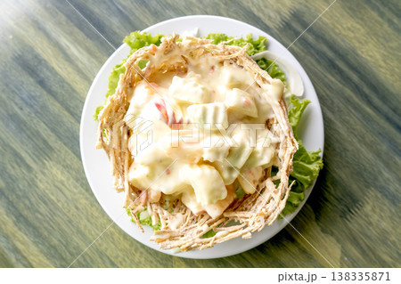 Top view of creamy fruit salad served in a crispy edible fried basket on a white plate with lettuce garnish. Appetizer dish on a green textured wooden background for a restaurant menu design. 138335871