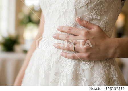ゴールドの結婚指輪をした花嫁の手がレースドレスに触れる 138337311