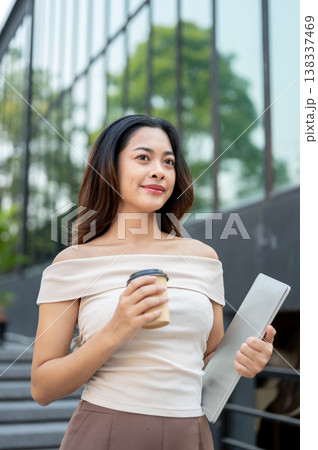 Pretty asian woman holding a laptop and coffee while standing or walking down stairs by the building 138337469