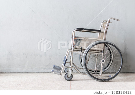 Empty wheelchair parked by wall in medical facility representing healthcare support mobility assistance recovery and disability access with clean minimal background space Empty wheelchair parked by wall in medical facility representing healthcare support mobility assistance recovery and disability access with clean minimal background space 138338412