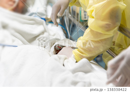 Healthcare worker in protective gown assisting patient in hospital bed with medical monitoring equipment showing clinical care treatment support and recovery in modern hospital environment 138338422