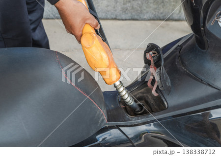 Hand holding fuel nozzle filling scooter tank close up Hand holding fuel nozzle filling scooter tank close up 138338712