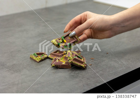 Woman's hand holds piece of Dubai chocolate on gray background. Green kadayif and pistachio spread with pistachio in trend dessert. Close-up, selective focus. High quality photo Woman's hand holds piece of Dubai chocolate on gray background. Green kadayif and pistachio spread with pistachio in trend dessert. Close-up, selective focus. High quality photo 138338747