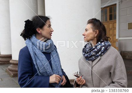 Mobility. Female friends strolling outdoors in cool season urban environment wearing coats and scarves communicating while moving through park area. Mobility. Female friends strolling outdoors in cool season urban environment wearing coats and scarves communicating while moving through park area. 138338760