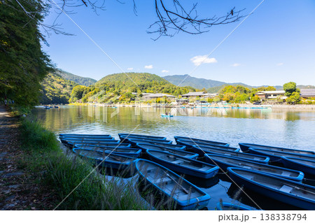 Traditional wooden boats moored on calm river under large tree in Kyoto with Togetsukyo bridge in background, Japan  138338794