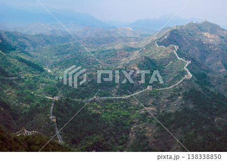 Historic of Great Wall fortification lines rugged terrain with winding path descending toward watchtowers emphasizing scale of ancient structure, Simatai, Beijing, China Historic of Great Wall fortification lines rugged terrain with winding path descending toward watchtowers emphasizing scale of ancient structure, Simatai, Beijing, China 138338850