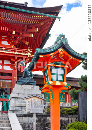 Fox statue with red bib and symbolic key seated on stone pedestal at Fushimi Inari Shrine in Kyoto against blue sky, Japan 138338855