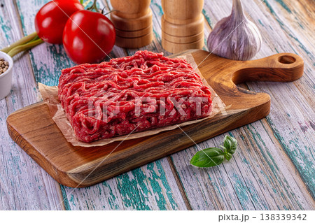 Fresh raw minced beef on a wooden cutting board with tomatoes, garlic, and basil. Fresh raw minced beef on a wooden cutting board with tomatoes, garlic, and basil. 138339342