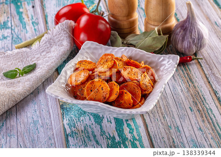 Bowl of baked carrot slices with herbs, spices, and fresh vegetables on a rustic wooden table. Bowl of baked carrot slices with herbs, spices, and fresh vegetables on a rustic wooden table. 138339344