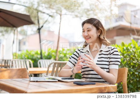 Pretty asian woman talking to video call on laptop aside book while sitting at table in garden cafe. 138339798