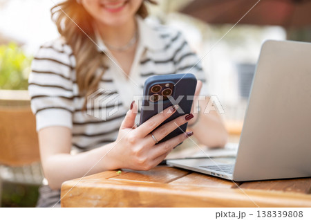 Close up of blurred woman looking at phone holding over laptop while sitting at wooden table in cafe Close up of blurred woman looking at phone holding over laptop while sitting at wooden table in cafe 138339808