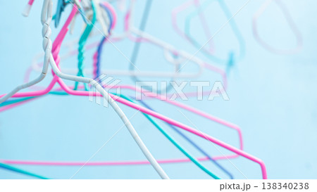 Close up of colorful wire clothes hangers in pastel pink blue and white against a light blue background with bokeh effect. Close up of colorful wire clothes hangers in pastel pink blue and white against a light blue background with bokeh effect. 138340238