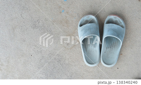 Top view of a pair of used light blue rubber slides or slippers placed on a textured grey concrete floor with copy space. 138340240