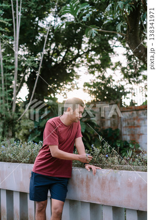 Southeast Asian man standing on bridge looking down at river wearing red shirt Southeast Asian man standing on bridge looking down at river wearing red shirt 138341971