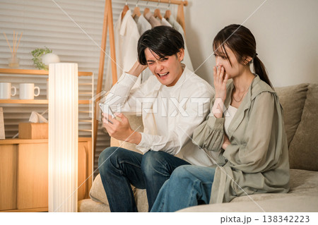 リビングのソファでスマホを見ながら困る,悩む若いアジア人夫婦 138342223