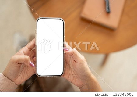 Close up of a woman's manicured hands holding white screen phone and sitting at wooden table in cafe Close up of a woman's manicured hands holding white screen phone and sitting at wooden table in cafe 138343006