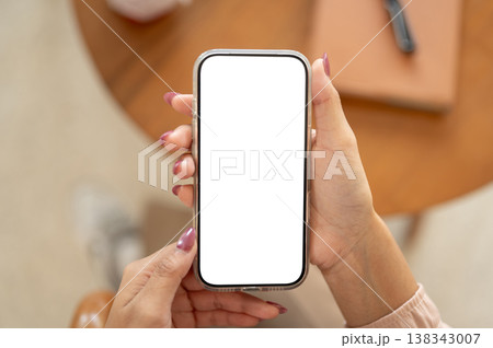 Close up of a woman's manicured hands holding blank screen phone and sitting at wooden table in cafe Close up of a woman's manicured hands holding blank screen phone and sitting at wooden table in cafe 138343007