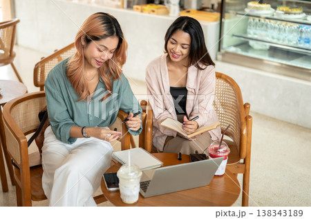 Asian woman student holding and showing a pen to her friend while working on group project in cafe. Asian woman student holding and showing a pen to her friend while working on group project in cafe. 138343189