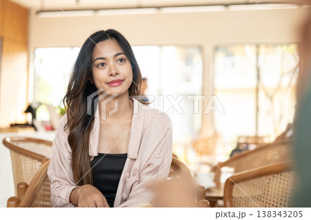 Pretty asian woman looking and listening to a friend or client on wooden chair while meet up in cafe Pretty asian woman looking and listening to a friend or client on wooden chair while meet up in cafe 138343205