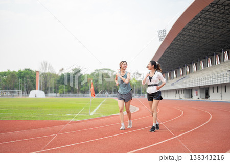 Athletic asian woman friends talking as running or jogging together on racetrack in sports stadium. Athletic asian woman friends talking as running or jogging together on racetrack in sports stadium. 138343216