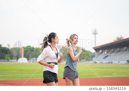 Athletic asian woman and friend in sportswear running or jogging together on racetrack in stadium. Athletic asian woman and friend in sportswear running or jogging together on racetrack in stadium. 138343219