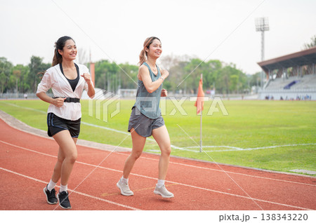Full body of athletic asian woman and friend in sportswear running together on racetrack in stadium. Full body of athletic asian woman and friend in sportswear running together on racetrack in stadium. 138343220