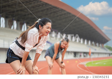 Tired asian woman and friend standing with hands on knees resting on running track in sports stadium Tired asian woman and friend standing with hands on knees resting on running track in sports stadium 138343231