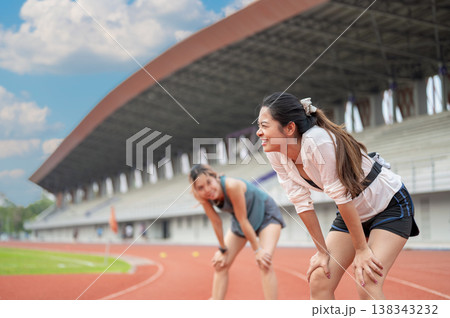 Asian woman and friend standing with hands on knees resting after running on track in sports stadium 138343232