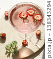 Pink strawberry margarita cocktail with sugar rim on marble tray. Fresh halved berries floating in sparkling rose drink with ice and sunlight shadows for summer party lifestyle. 138343294